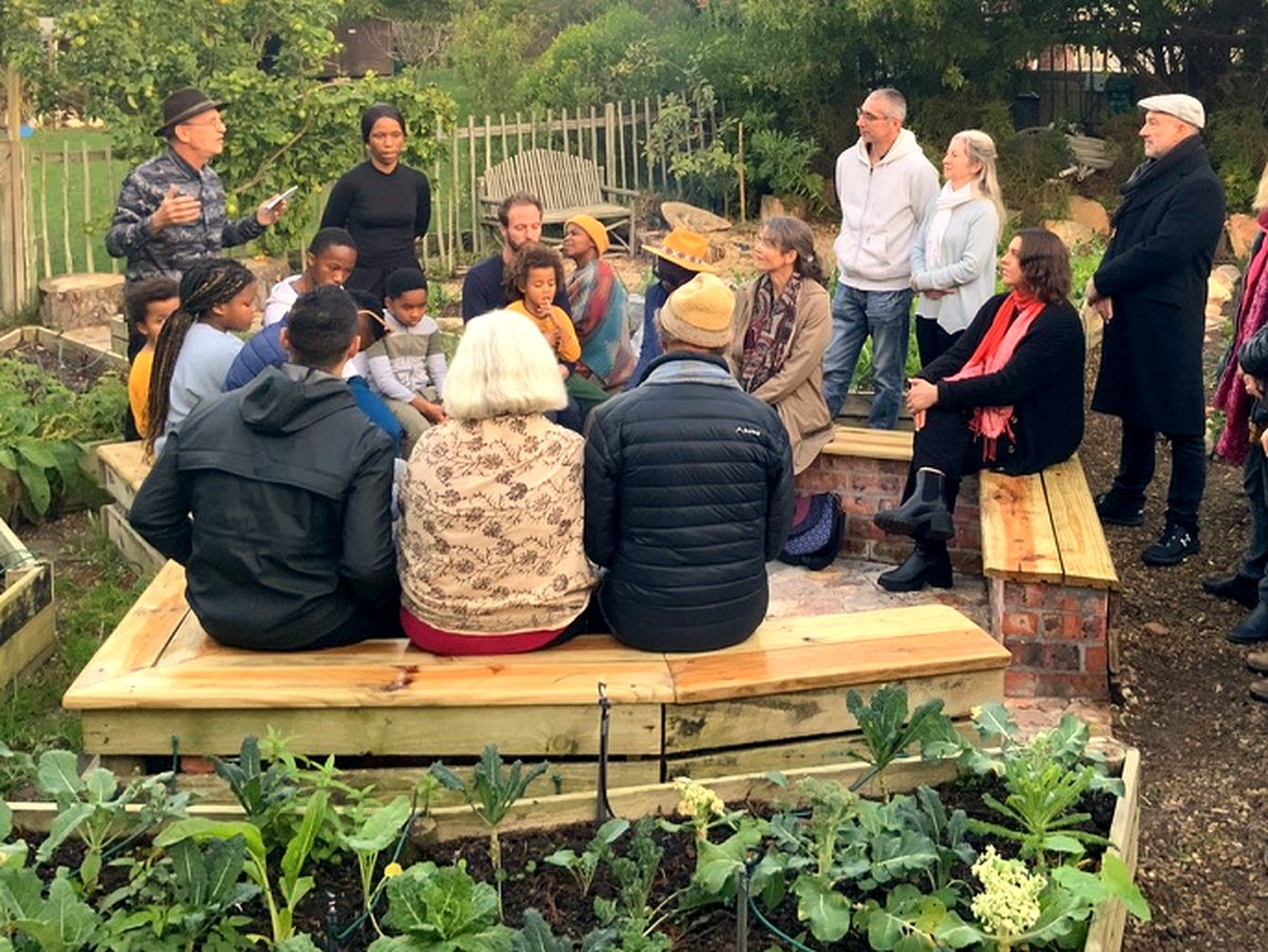 Dr. Raoul Goldberg speaking to a gathering around the fire pit in the vegetable garden